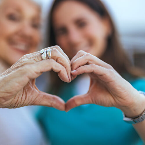 Two women forming a heart shape with their hands, symbolizing compassionate home health care services, with a focus on elderly and patient-centered care.
