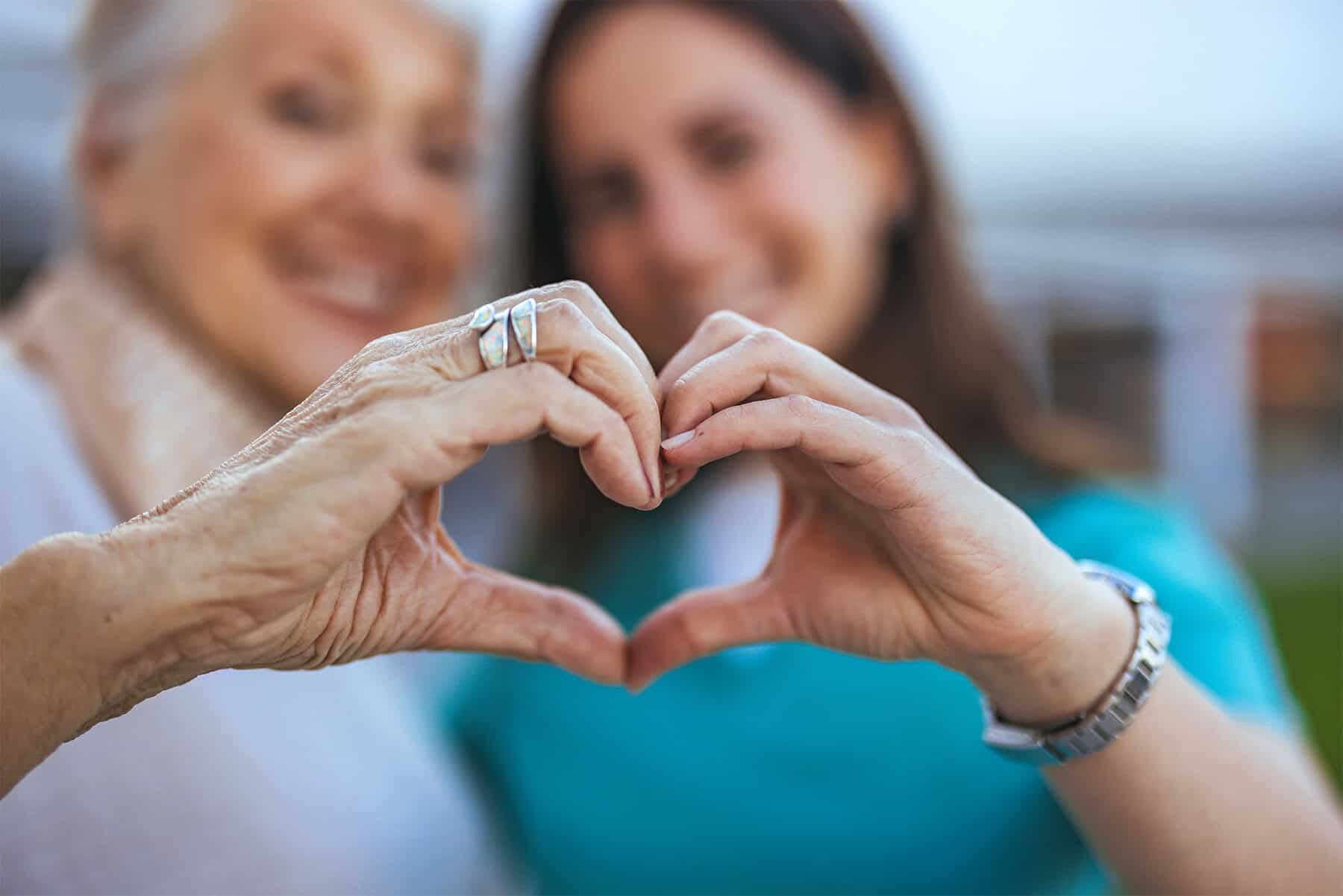 Two women forming a heart shape with their hands, symbolizing compassionate home health care services, with a focus on elderly and patient-centered care.