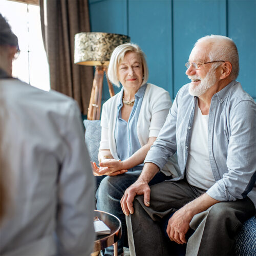 Elderly couple receiving home health care consultation from a healthcare professional in a cozy living room setting. Focus on compassionate senior care and support services.