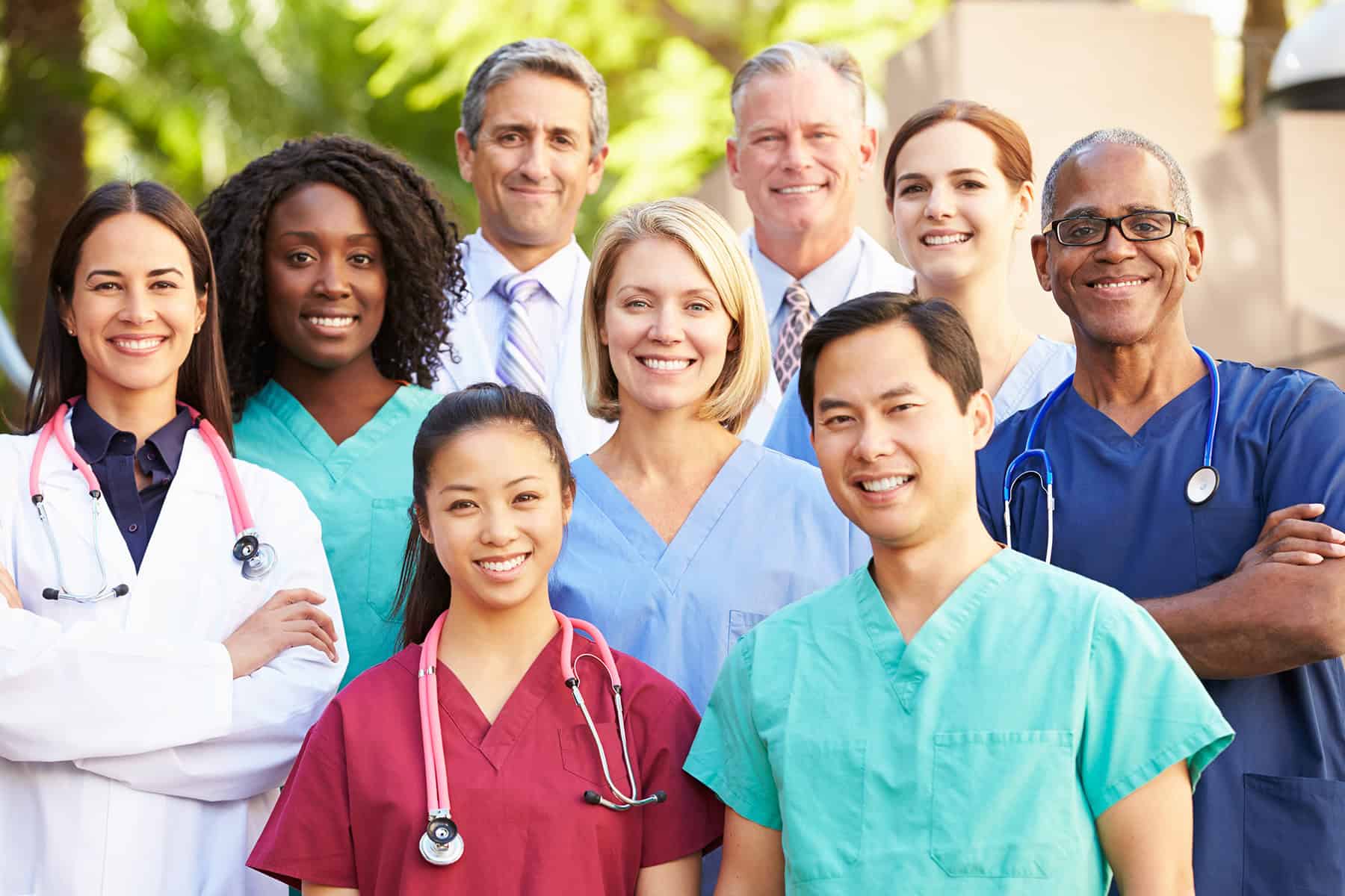Diverse group of healthcare professionals including nurses, doctors, and caregivers smiling outdoors, representing compassionate home health services and patient-centered care.
