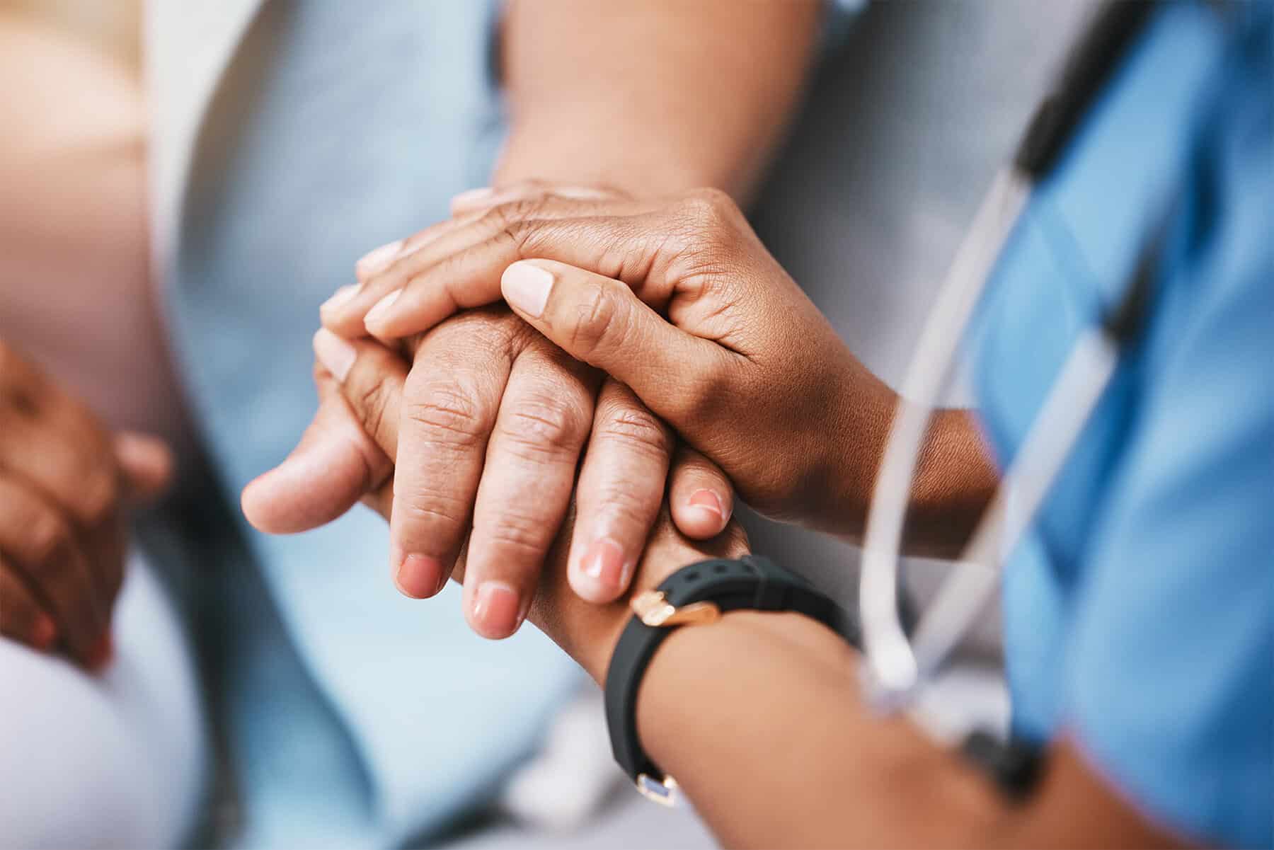 Close-up of a healthcare professional holding an elderly patient's hand, emphasizing compassionate home health care and patient support services.
